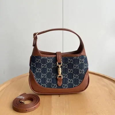 Denim hobo bag with a tan leather handle, upright on a pale chair