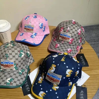 Half a dozen patterned baseball caps stacked on a desk beside a coffee cup