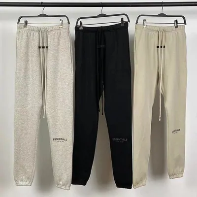 Three pairs of cuffed sweatpants on hangers against a white wall